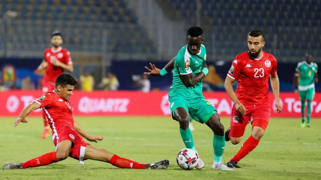 Tuniský Mohamed Drager se skluzem pokouší zastavit  Idrissu Gueyeho ze Senegalu