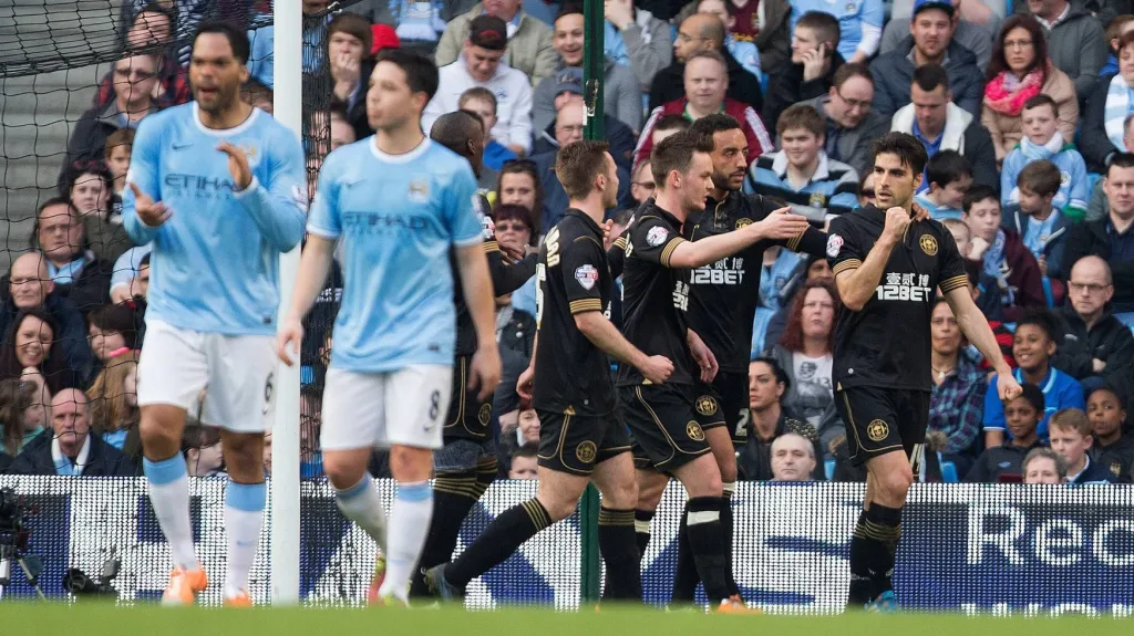 Zklamaní Lescott s Clichym a radující se fotbalisté Wiganu v pozadí