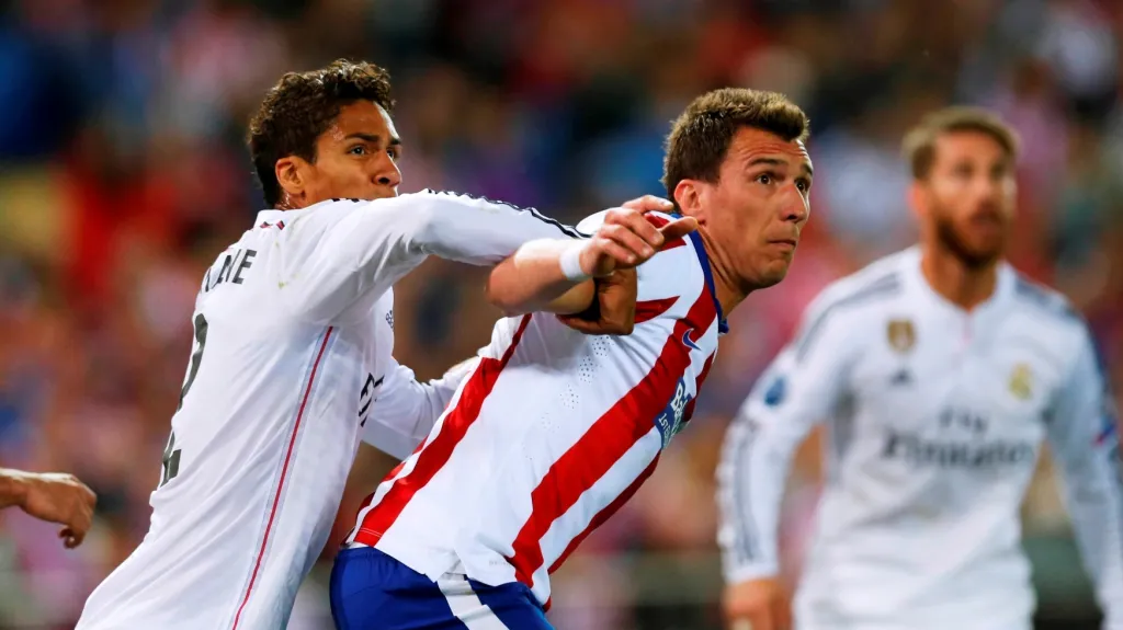 Mario Mandžukič z Atlética Madrid si drží na zádech obránce Realu Madrid Raphaëla Varana