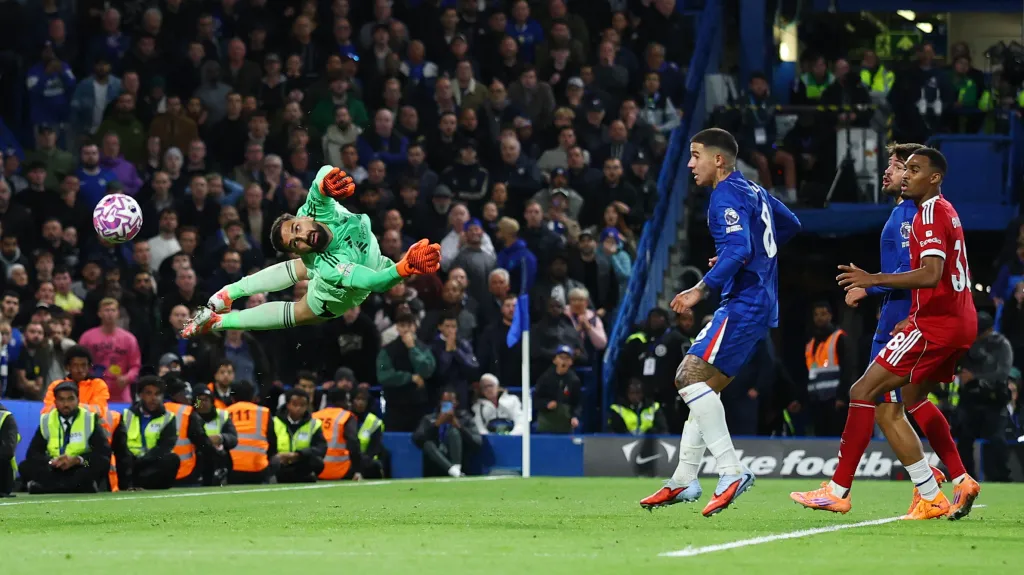 Brankář Liverpoolu Giorgi Mamardašvili letí vzduchem v utkání proti Chelsea