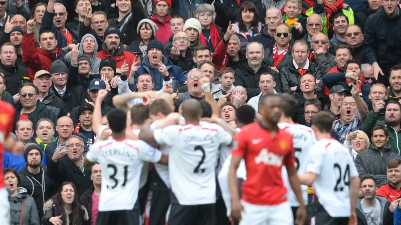 Radost fotbalistů Liverpoolu, v pozadí příznivci Manchesteru United