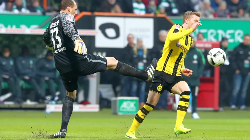 Brankář Brém Jaroslav Drobný fauluje unikajícího Marca Reuse z Dortmundu