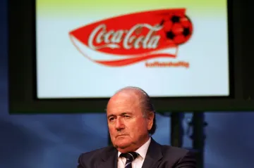 Logo společnosti Coca-Cola nad hlavou Seppa Blattera