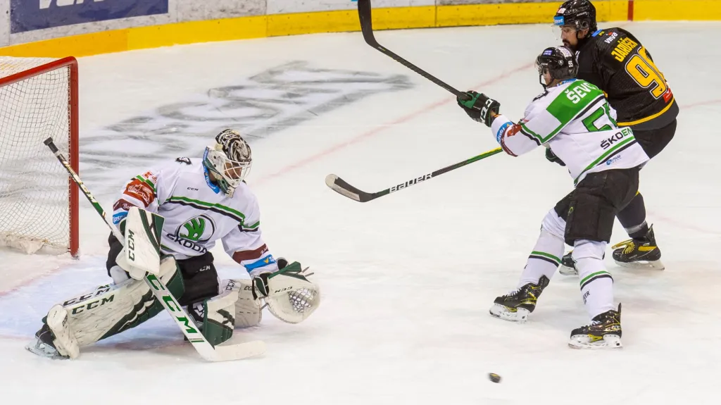 Mladoboleslavský gólman Jan Růžička chytá puk před dotírajícím Richardem Jarůškem z Litvínova