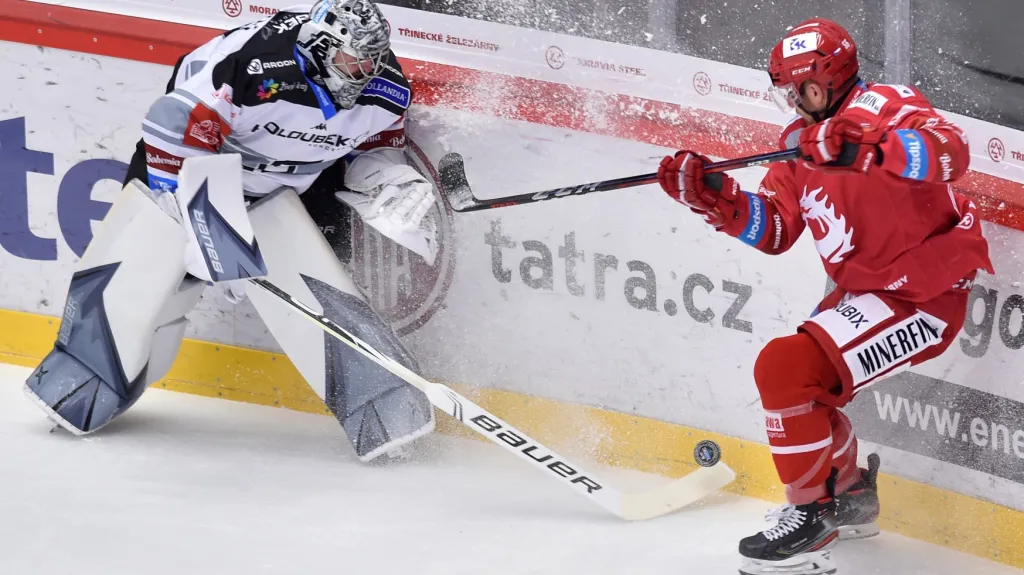 Karlovarský gólman Filip Novotný odehrává puk před Marianem Adámkem z Třinec