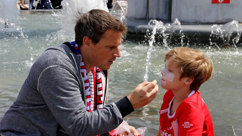 Otec maluje synovi na obličej švýcarskou vlajku